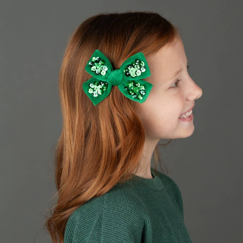 Young girl with a green hair clip featuring a shamrock design on a gray background