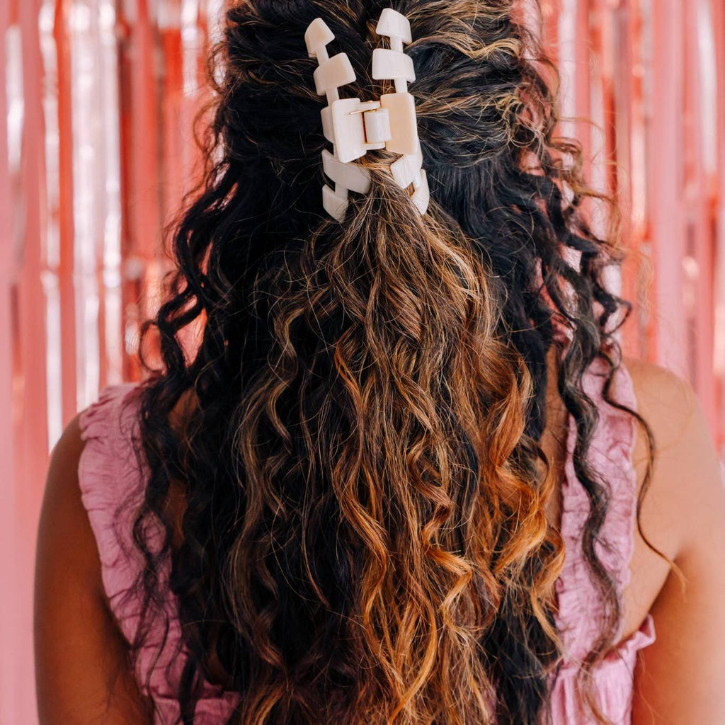 Person with long, wavy hair wearing a decorative hair clip against a pink tinsel background