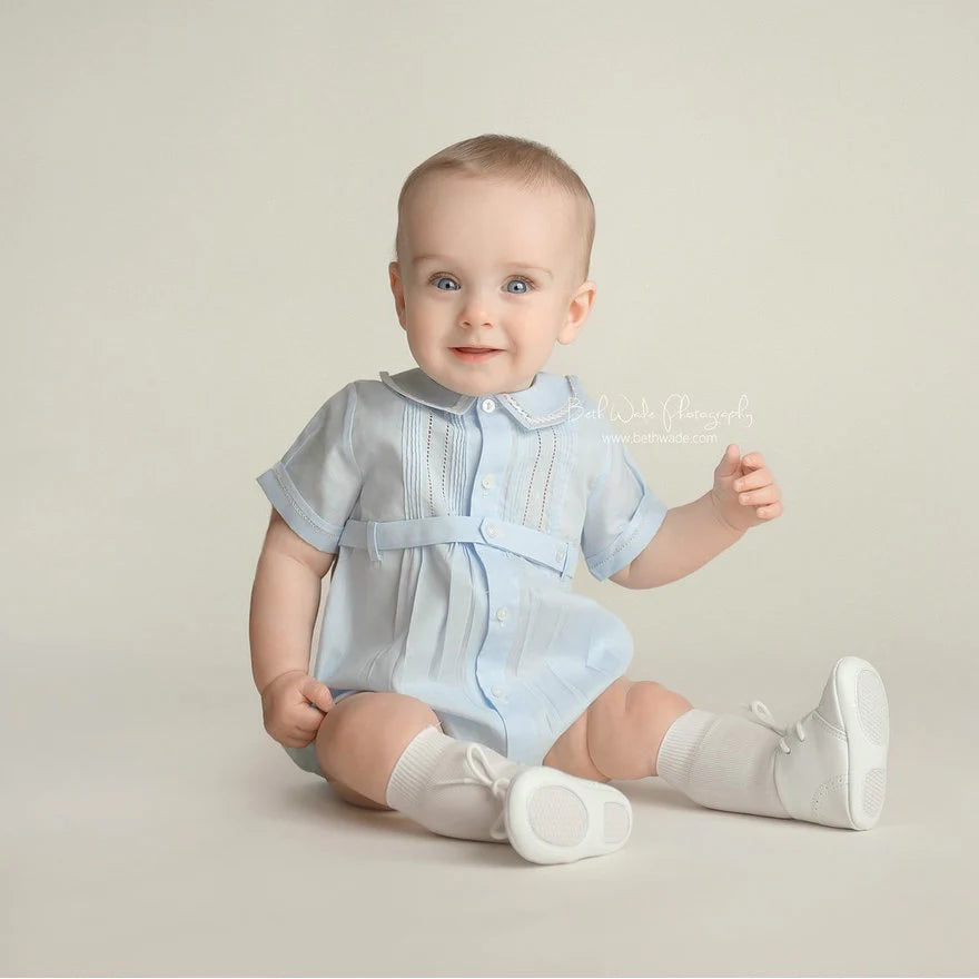 Baby wearing a light blue outfit with a belt on a beige background