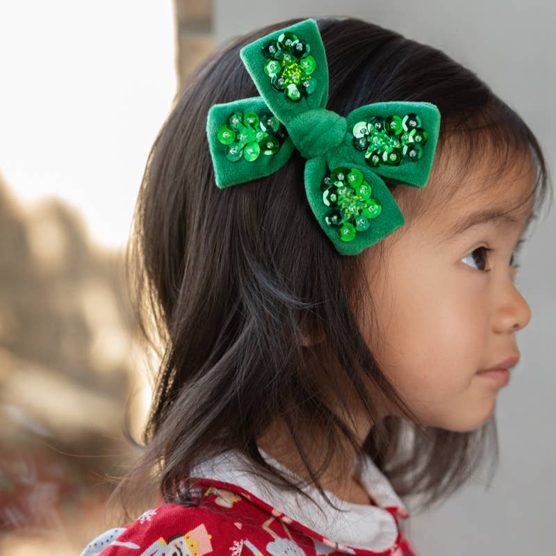 Child wearing a red garment with a white collar and a green bow headband.