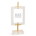 A mini easel with a clear acrylic panel and a gold-colored iron frame, standing on a solid surface.