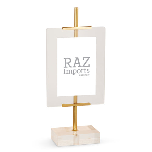 A mini easel with a clear acrylic panel and a gold-colored iron frame, standing on a solid surface.