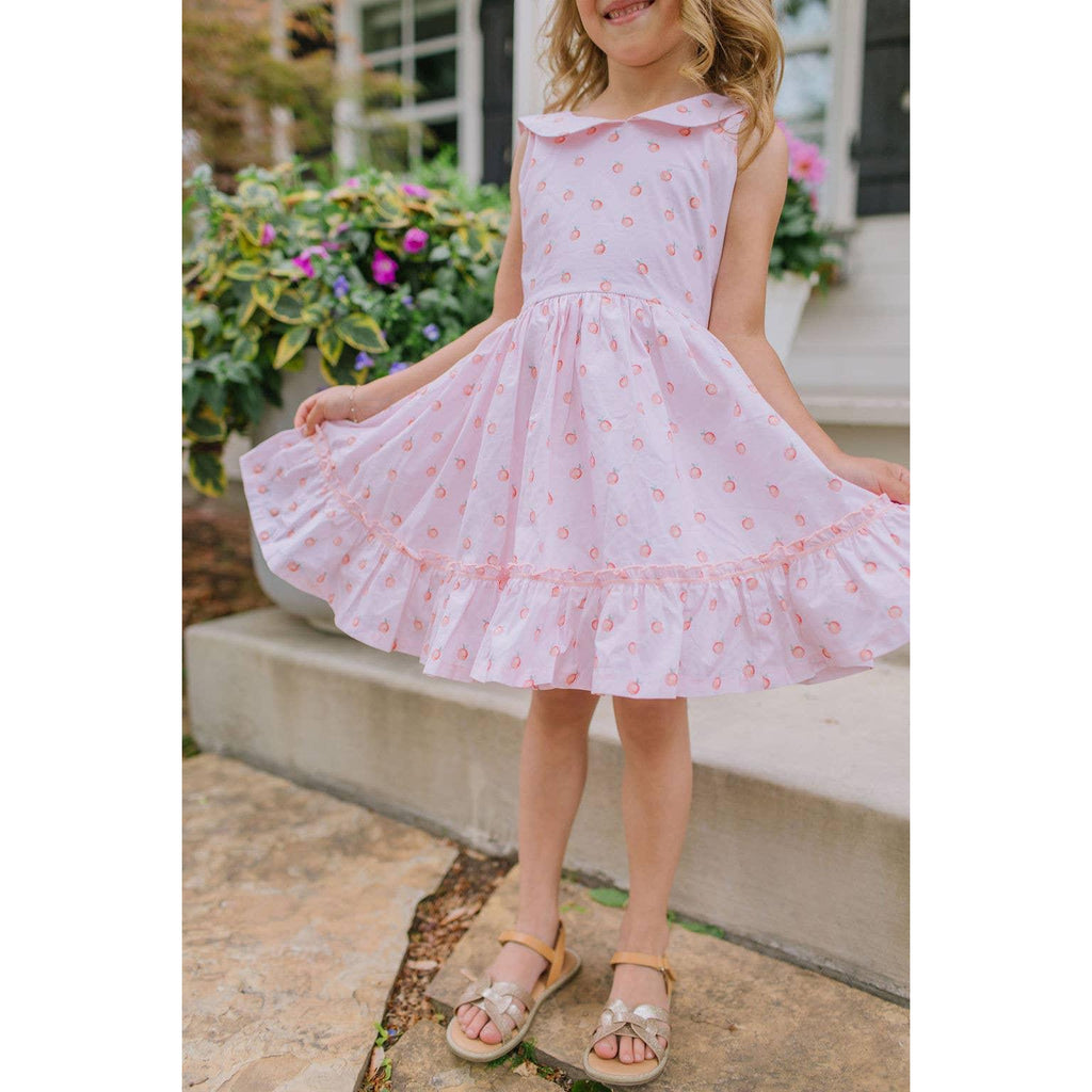 Child wearing a pink floral dress standing outdoors with flowers in the background