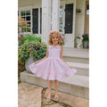 Young girl in a pink dress standing on a porch with flowers and a house in the background