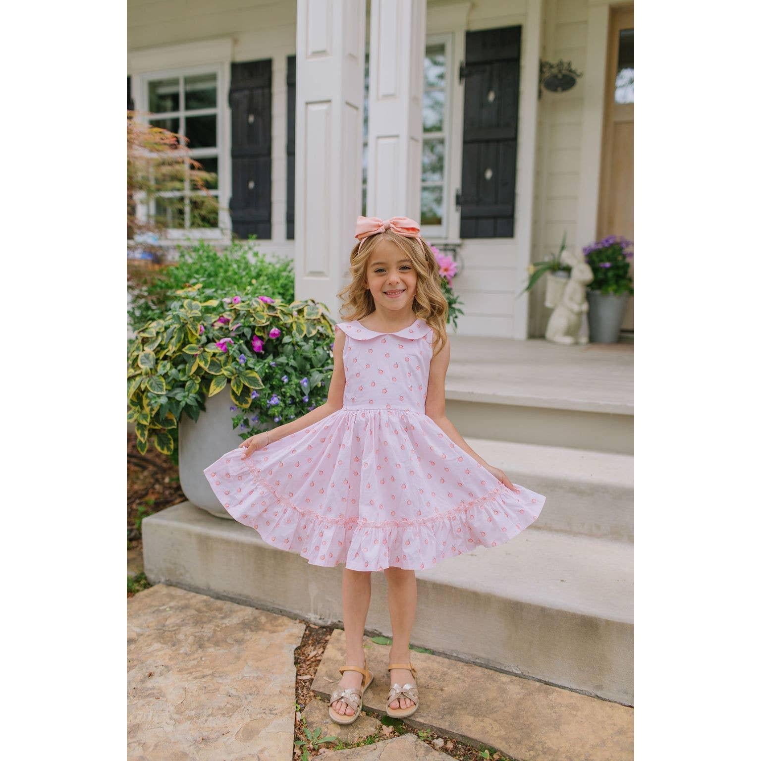 Young girl in a pink dress standing on a porch with flowers and a house in the background