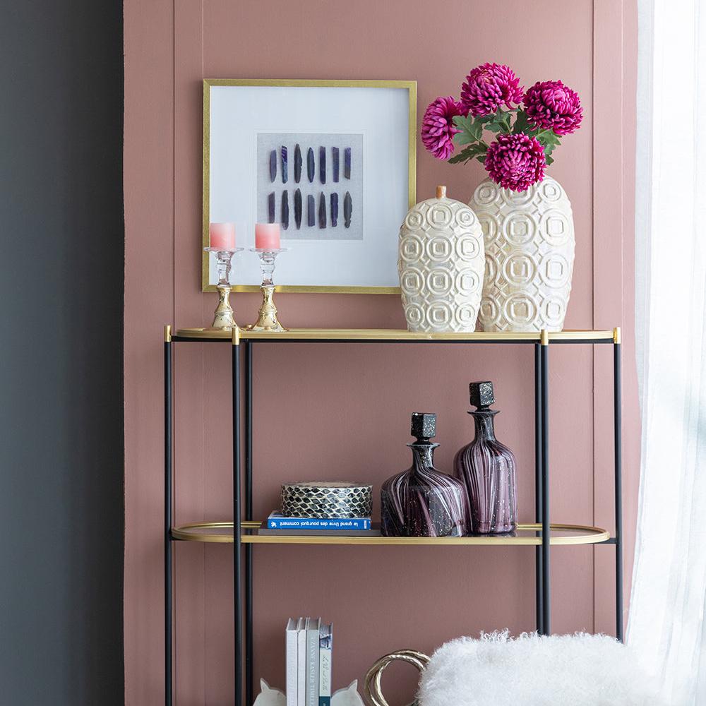 Decorative shelf with books, vases, and a vase with flowers against a pink wall.