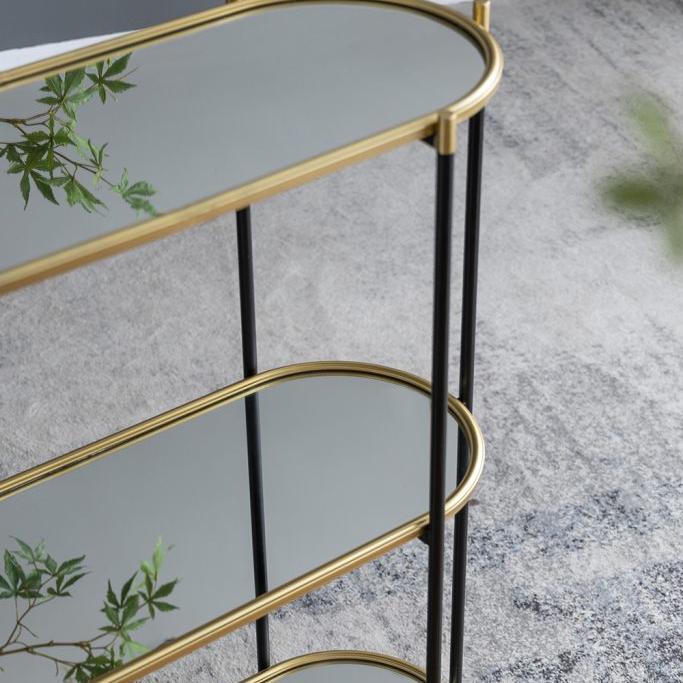 Two-tiered glass table with gold frames on a gray floor.