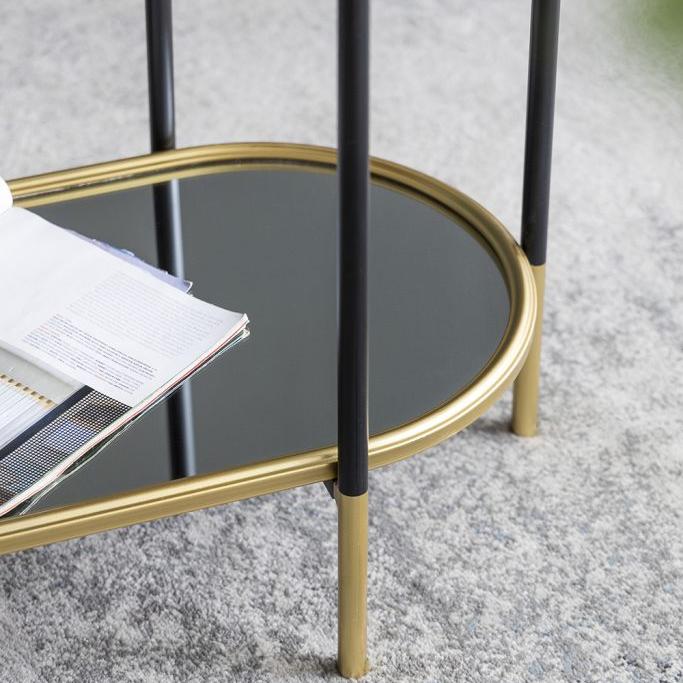 Small round table with black metal legs and gold metal frame on a textured surface.