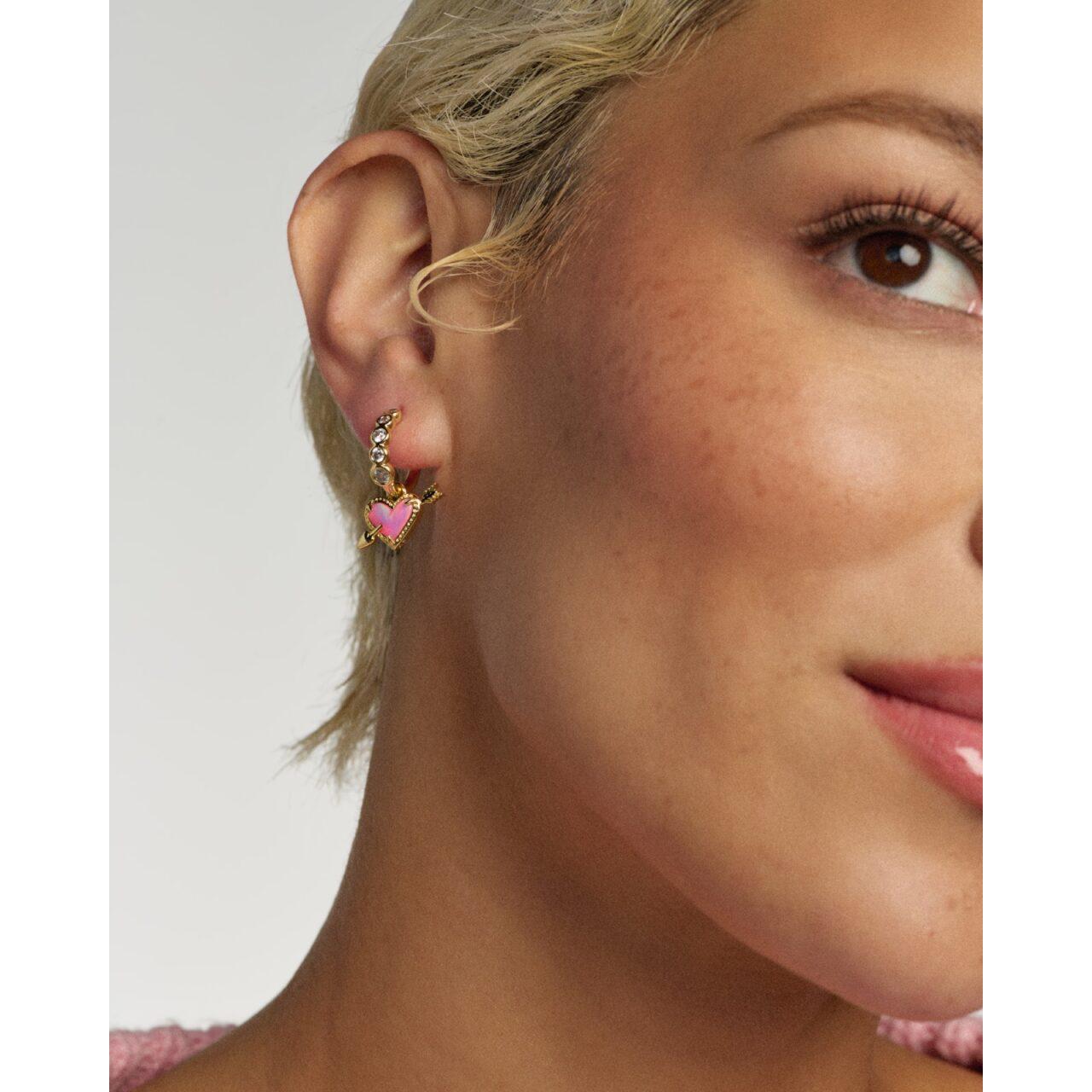 Close-up of a woman wearing a gold earring with a pink heart design.