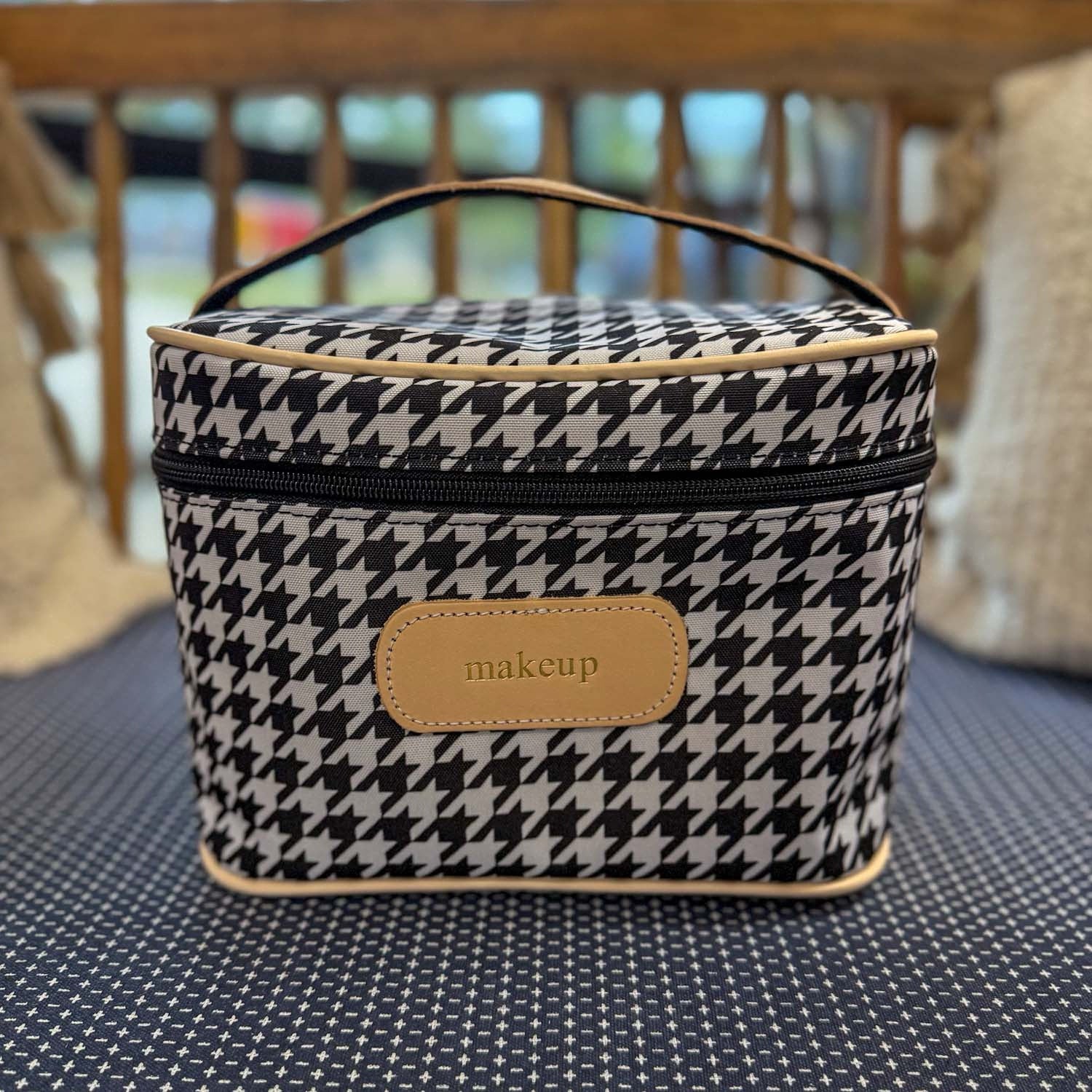 Houndstooth patterned makeup bag with a brown label on a textured surface.