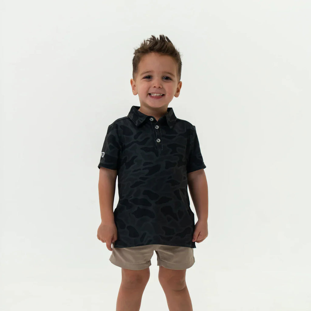 Child wearing a Burlebo black camo Polo and Khaki shorts on a white background