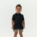 Child wearing a Burlebo black camo Polo and Khaki shorts on a white background