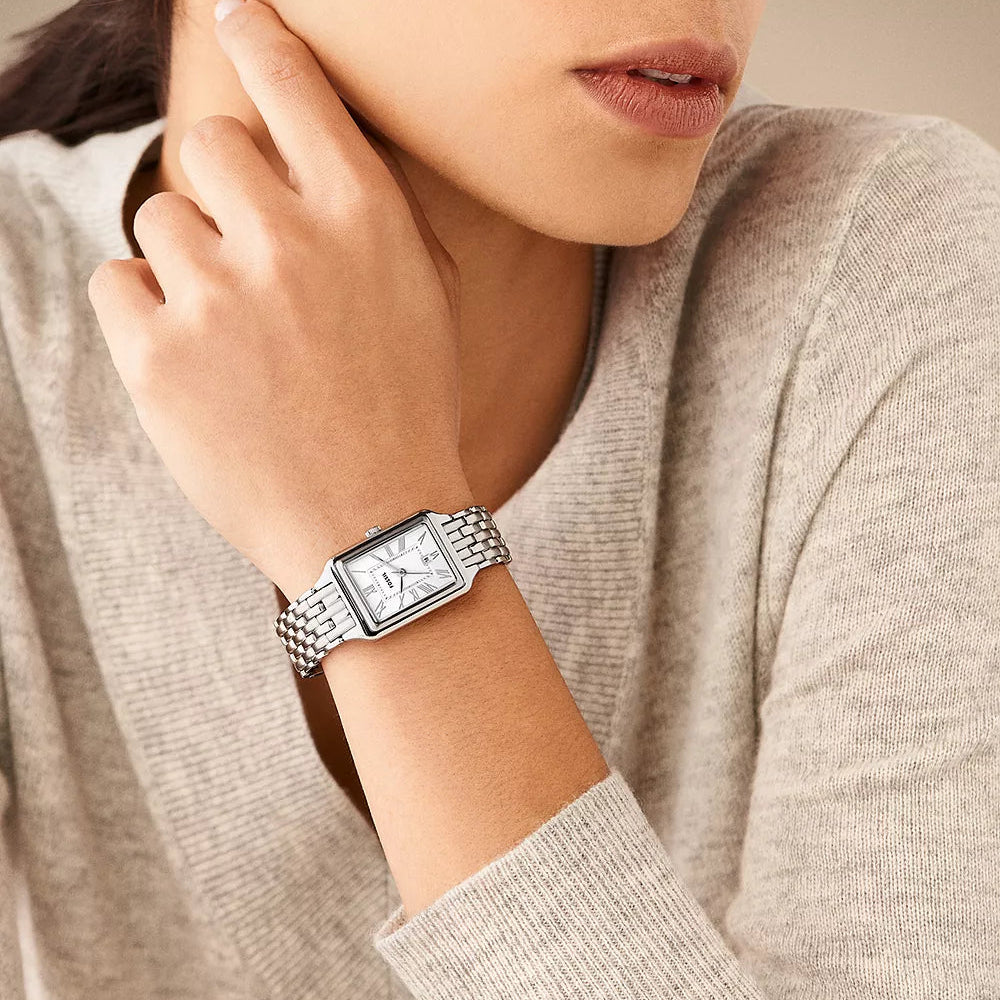 Person wearing a silver Fossil watch with a neutral background