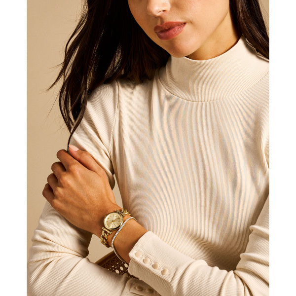 Woman wearing a beige sweater and gold Fossil watch with a neutral background