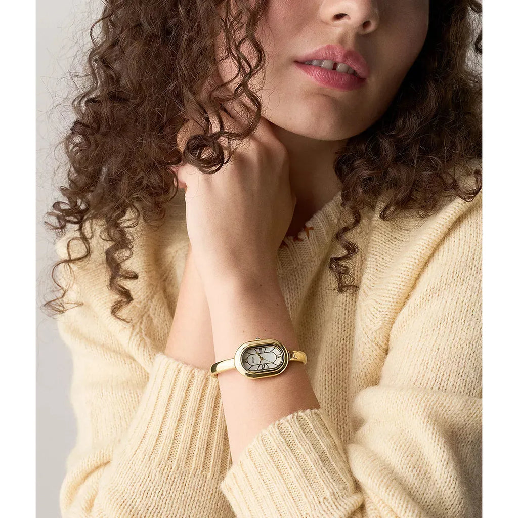 Woman wearing a gold Fossil watch with a neutral background