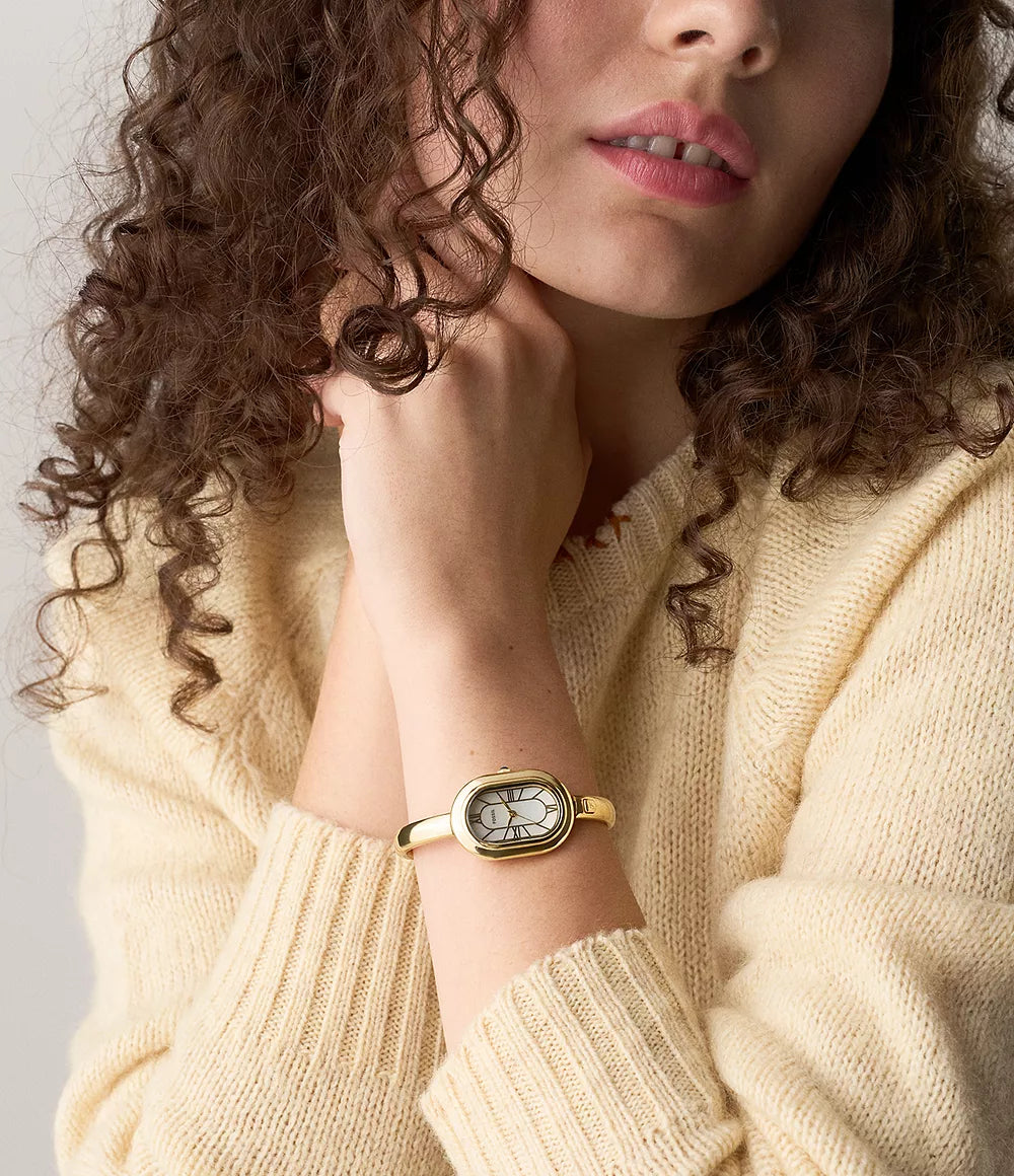 Woman wearing a gold Fossil watch with a neutral background