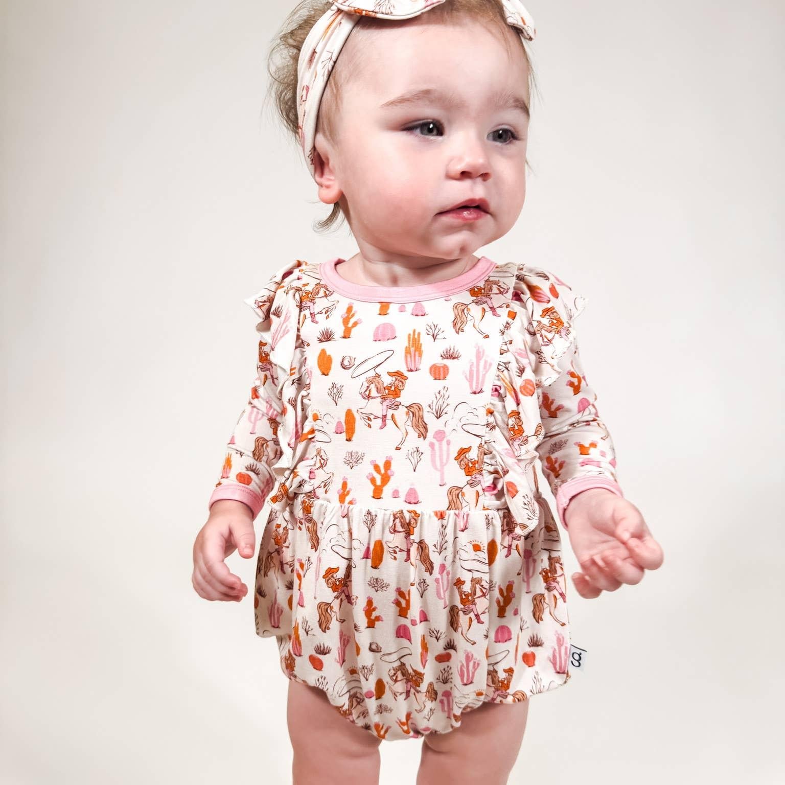 Baby wearing a western floral romper and headband on a plain background