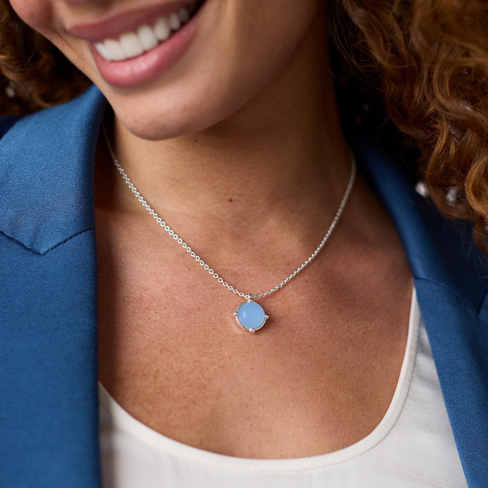 Close-up of a person wearing a silver necklace with a blue pendant.