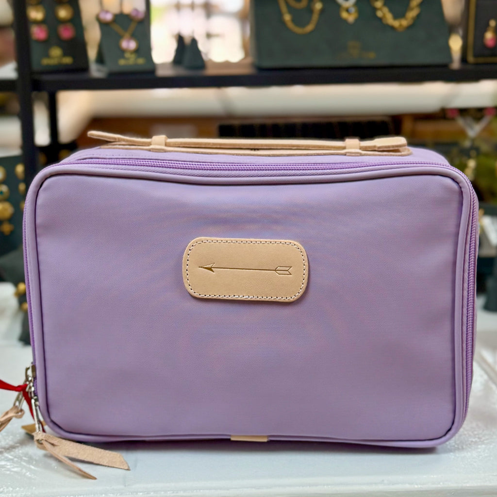 A purple travel kit with a zipper and a tan handle, displayed on a table with various items in the background.