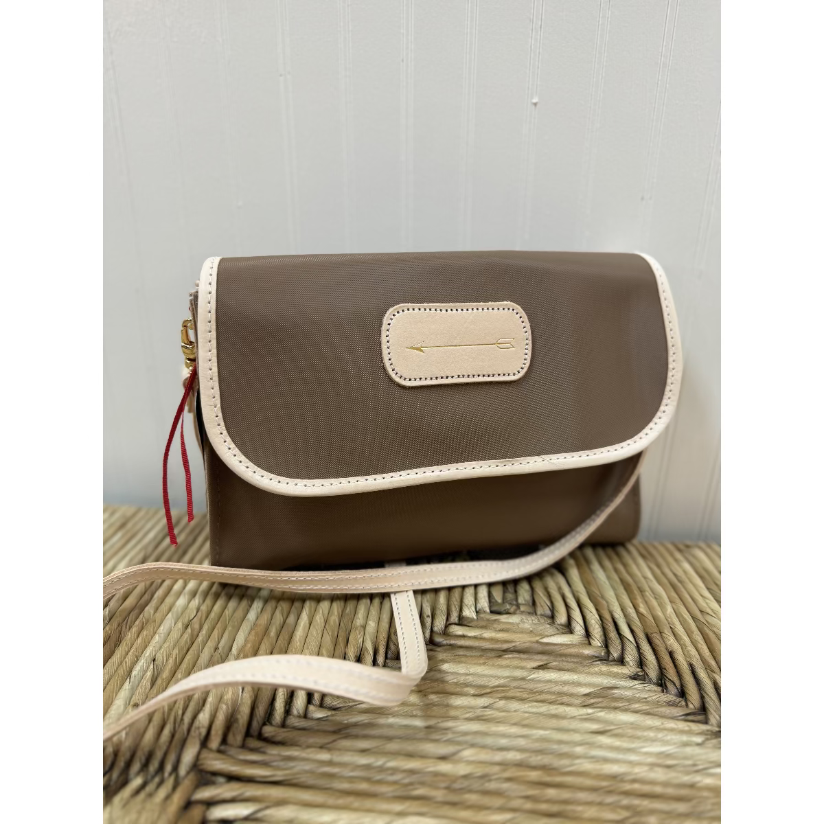 A brown and beige crossbody purse with a snap closure, a magnetic clasp, and a detachable strap, displayed against a woven background.