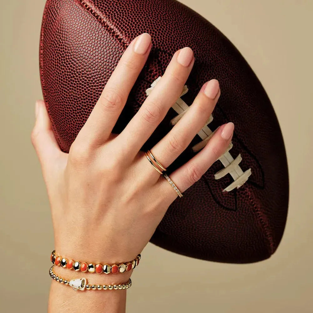 Hand holding a football with bracelets on a beige background