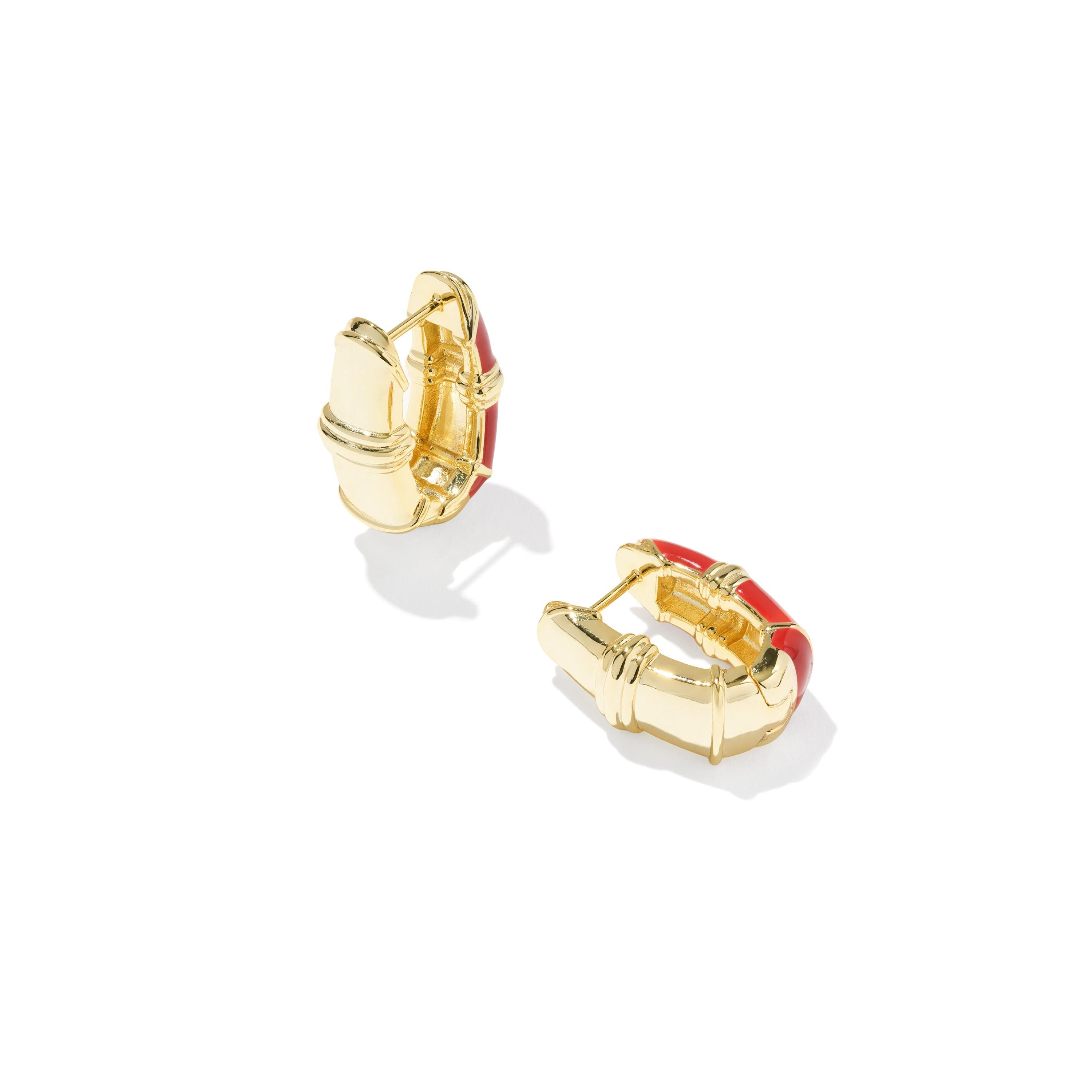 The back view of a pair of Kendra Scott gold huggie hoop earrings with curved red enamel inlays.
