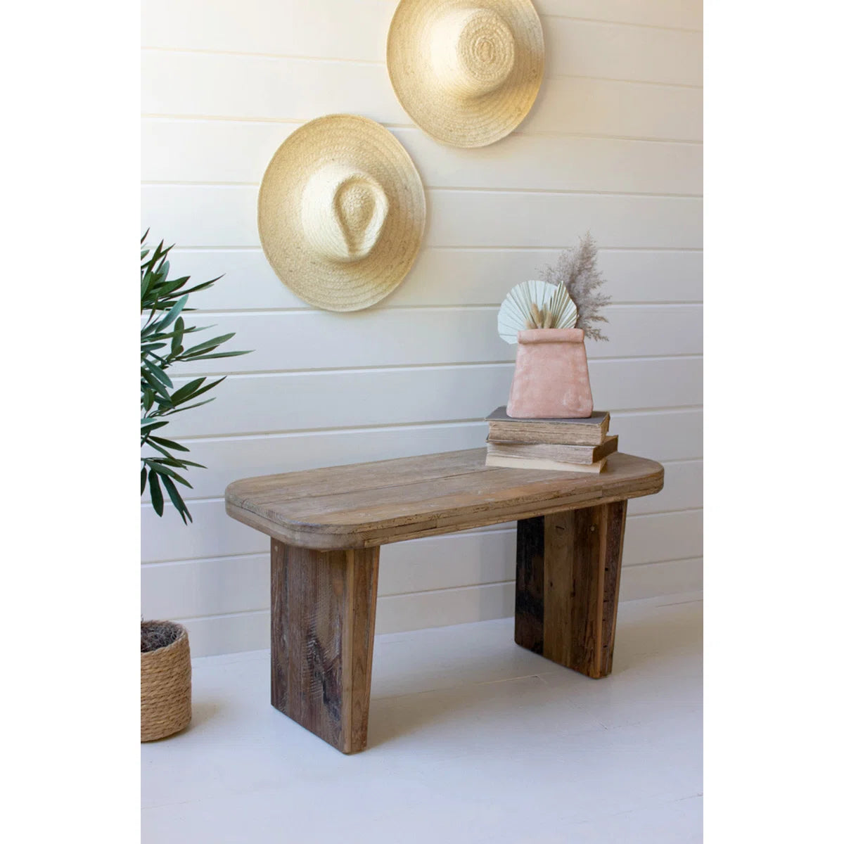 Wooden bench with decorative items against a white wall with straw hats.