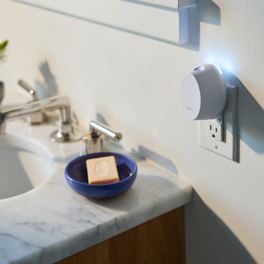 Pura Mini smart plug device on a wall socket next to a sink with soap.