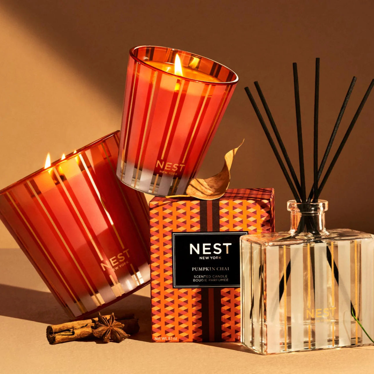 Two red candles and a diffuser with 'NEST' branding on a warm-toned background.