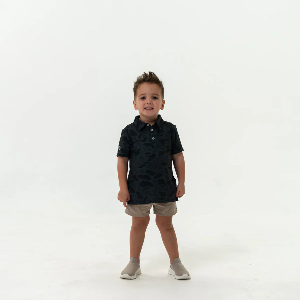 Child wearing a Burlebo black camo Polo and Khaki shorts on a white background