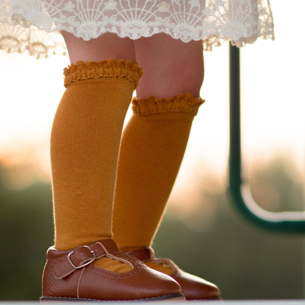 Child's legs wearing mustard-colored knee-high socks and brown shoes with a blurred background
