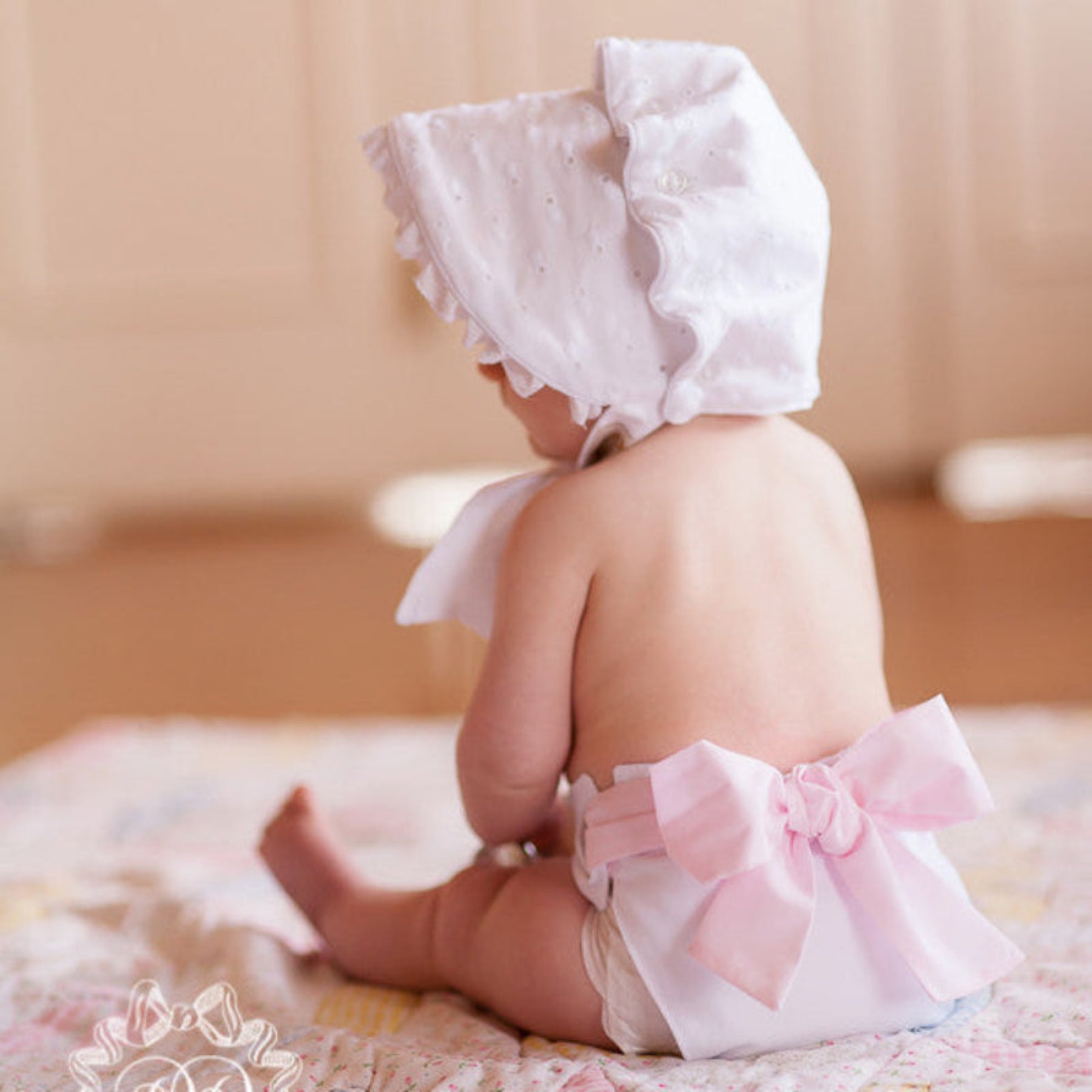 Baby wearing a white bonnet and pink bow diaper cover on a neutral background