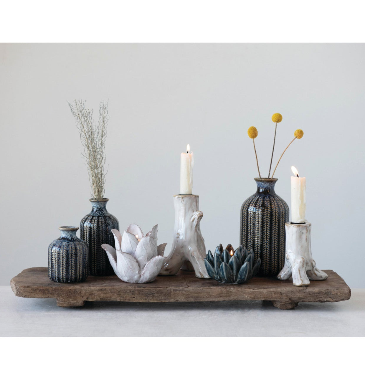 Decorative arrangement with vases, candles, and a wooden platform on a light background