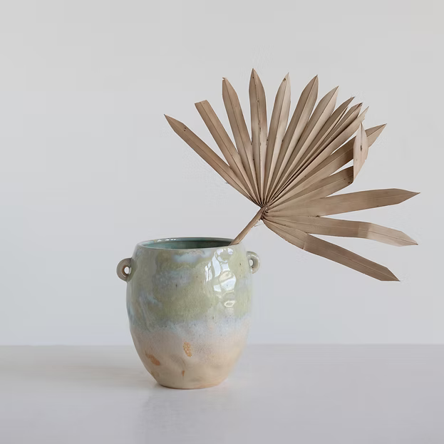 Ceramic vase with a textured surface and a dried palm leaf on a light background
