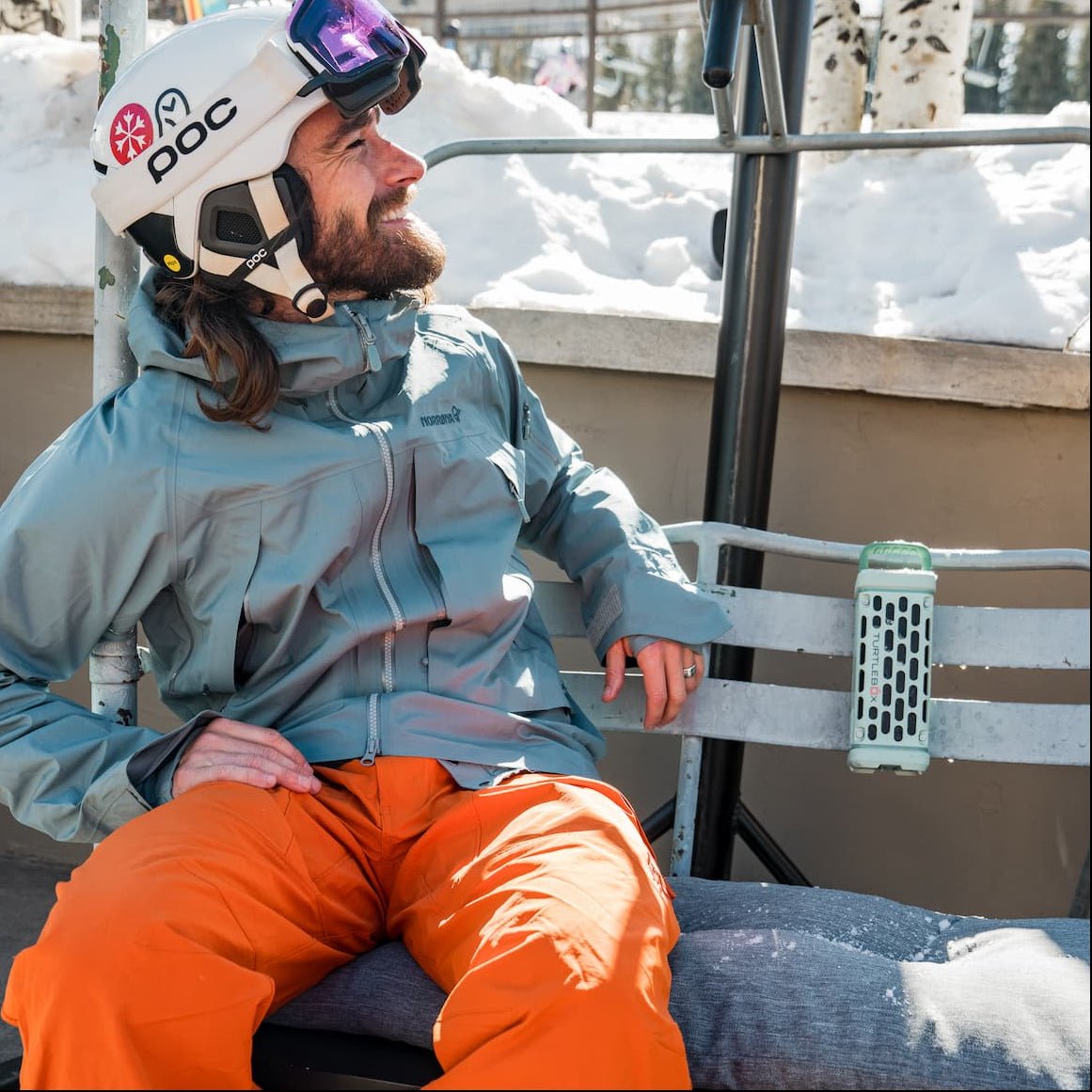 Person in ski gear sitting on a chairlift with snow and trees in the background
