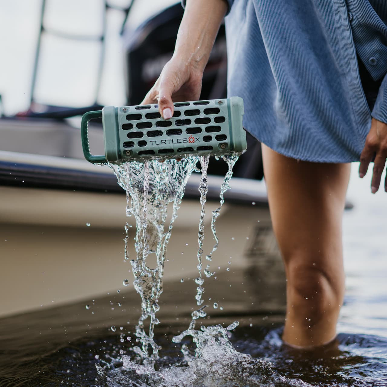 Person holding a waterproof speaker in water near a boat
